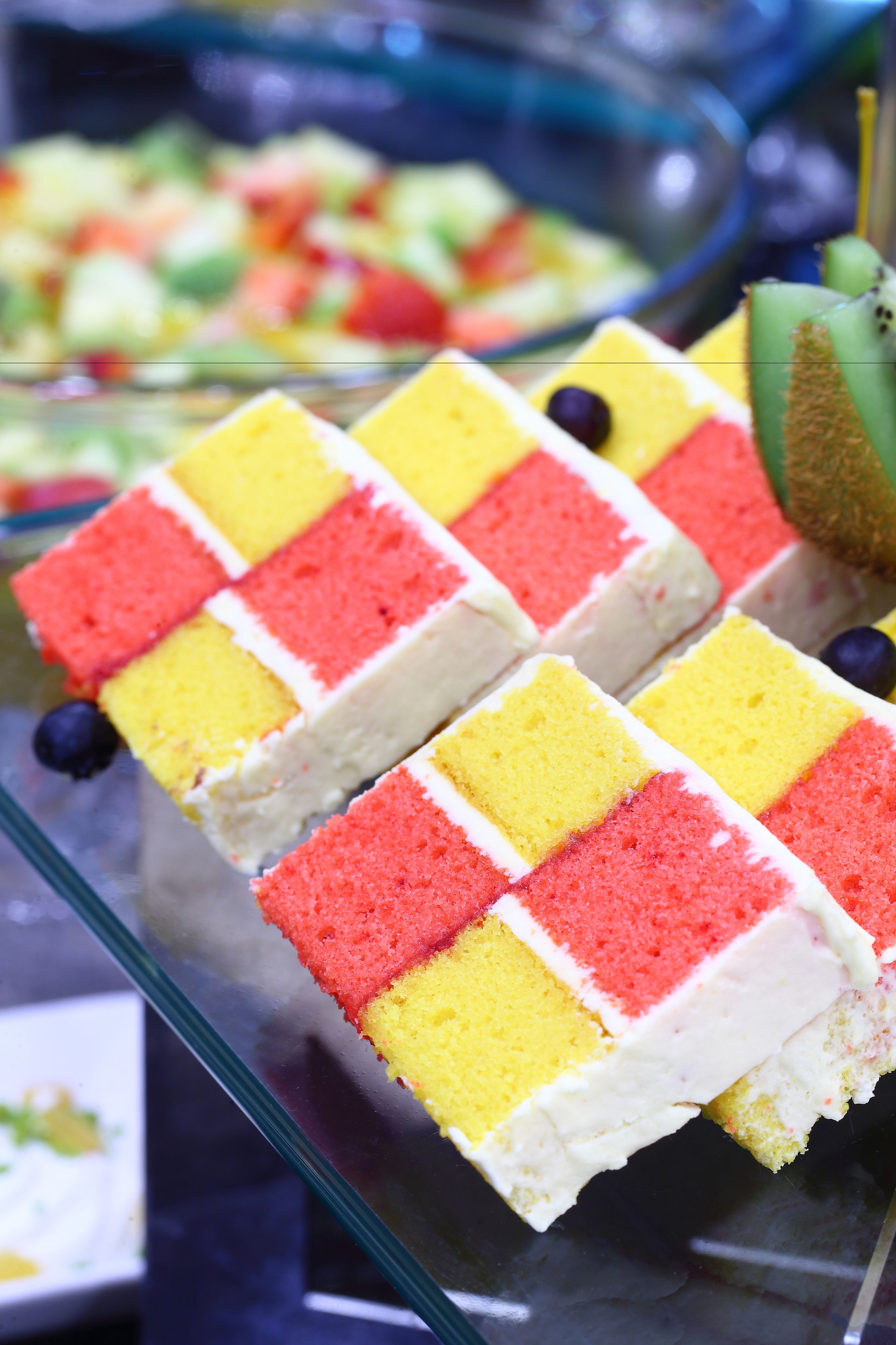 A glass display case with a layered cake and a kiwi.