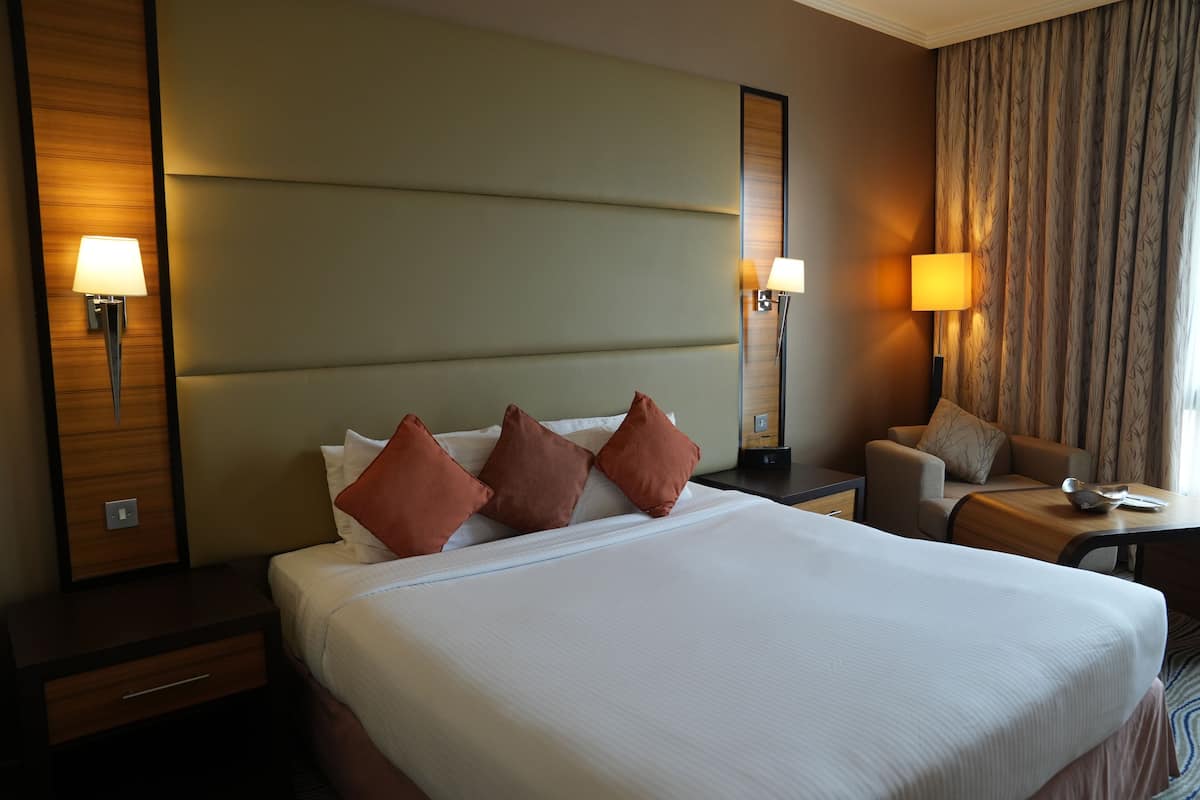 Una habitación de hotel con una cama grande, dos mesitas de noche, un sofá y una lámpara.