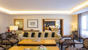 A hotel room with a sofa, armchairs, a coffee table, and a TV. There is a framed picture on the wall and a lamp on the side table.