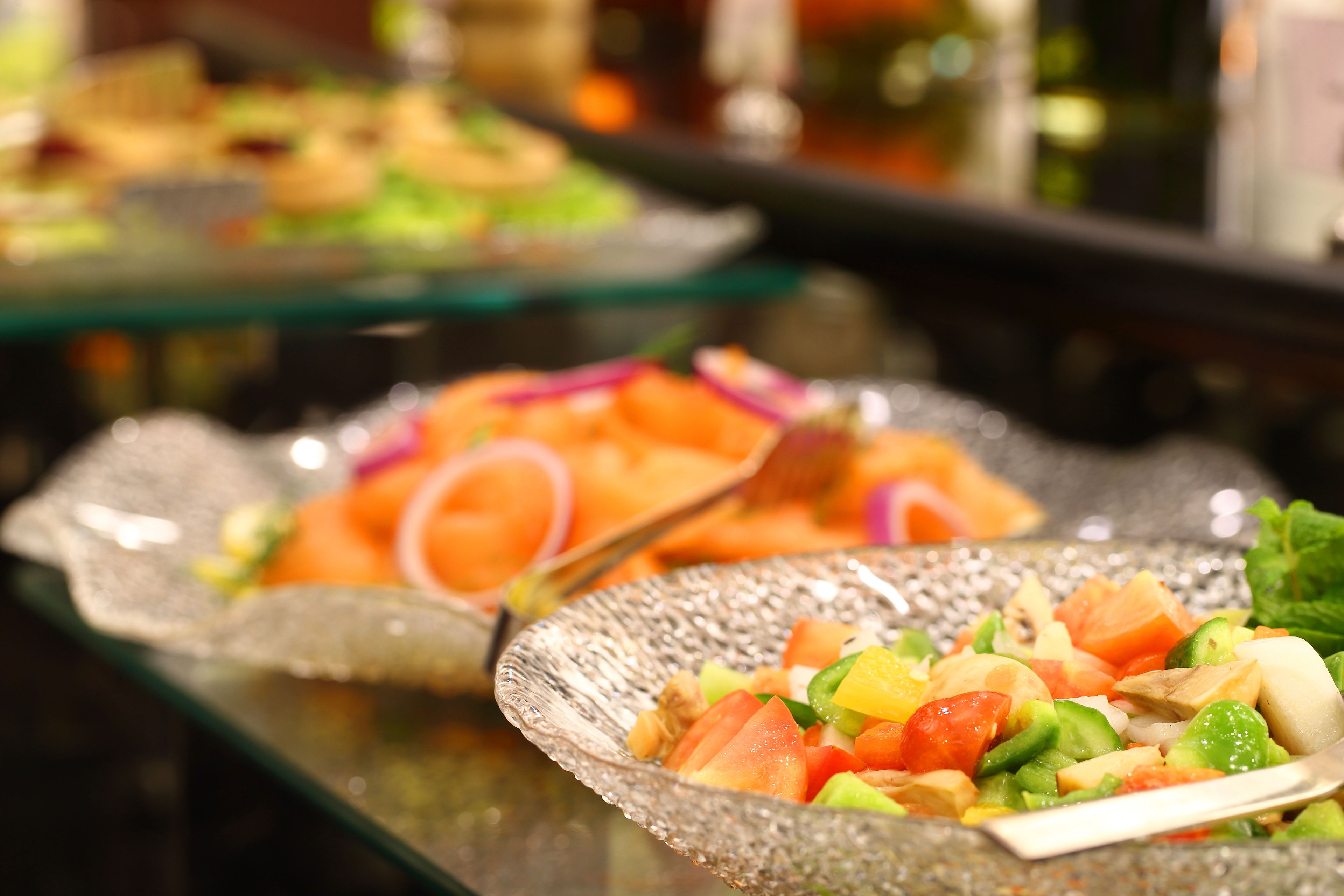 Un bufé con diversos platos, incluyendo una ensalada de verduras y fruta, y un tazón de vidrio con una cuchara.