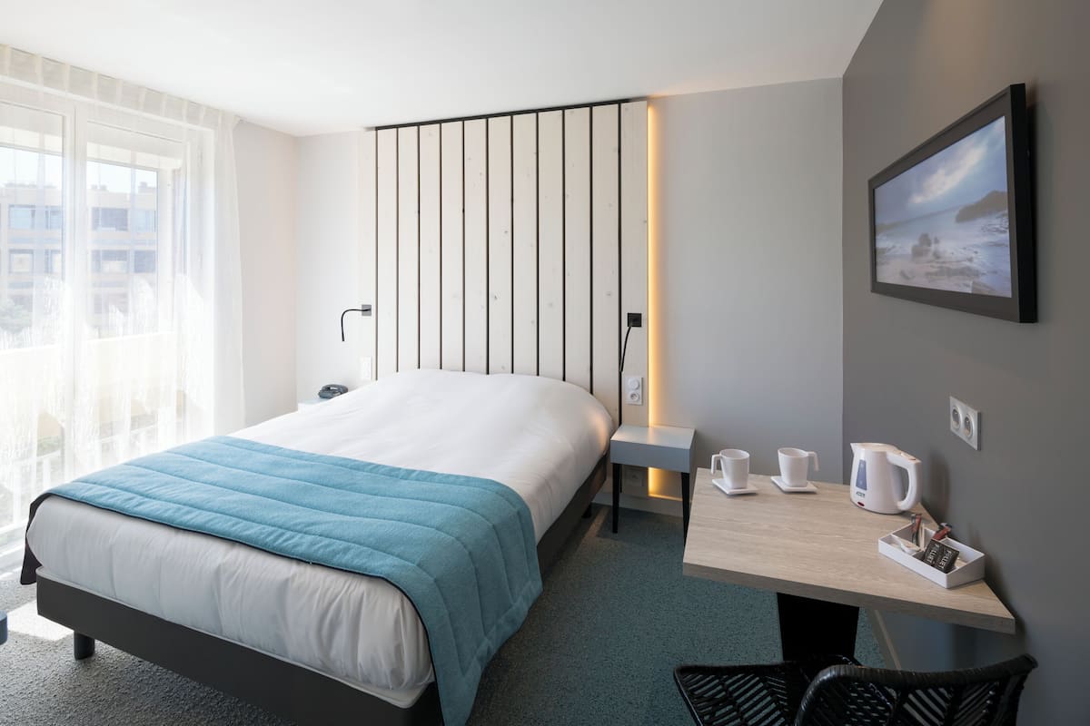 A modern hotel room with a large bed, bedside table, and a view of the city.