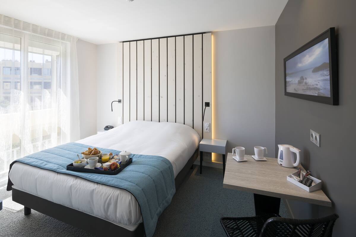 Une chambre d’hôtel comprenant un lit, une table de chevet et un bureau avec une chaise.