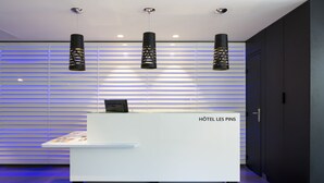 Un mostrador de recepción con un letrero que dice "HÔTELLES PINS" en un moderno vestíbulo de hotel con iluminación horizontal y paredes de tonos oscuros.