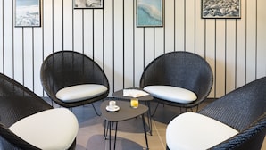 Una habitación con dos sillones de mimbre, una mesita con una taza y un vaso de zumo de naranja, y tres cuadros en la pared.