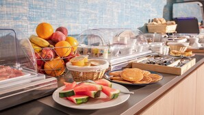 Un bufé con diversas opciones de comida, entre ellas frutas, panqueques y sándwiches.
