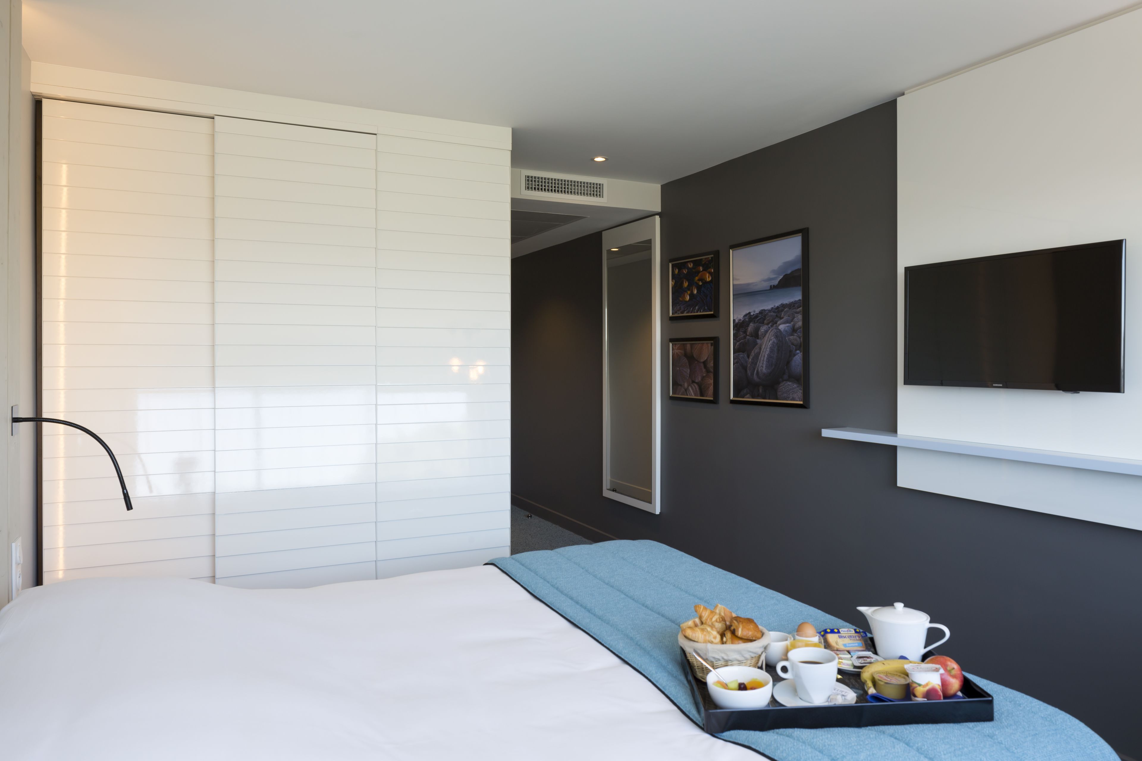 Una habitación de hotel moderna con cama, bandeja de desayuno, televisor de pantalla plana y un espejo grande.