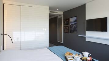 A modern hotel room with a bed, a breakfast tray, a flat-screen TV, and a large mirror.
