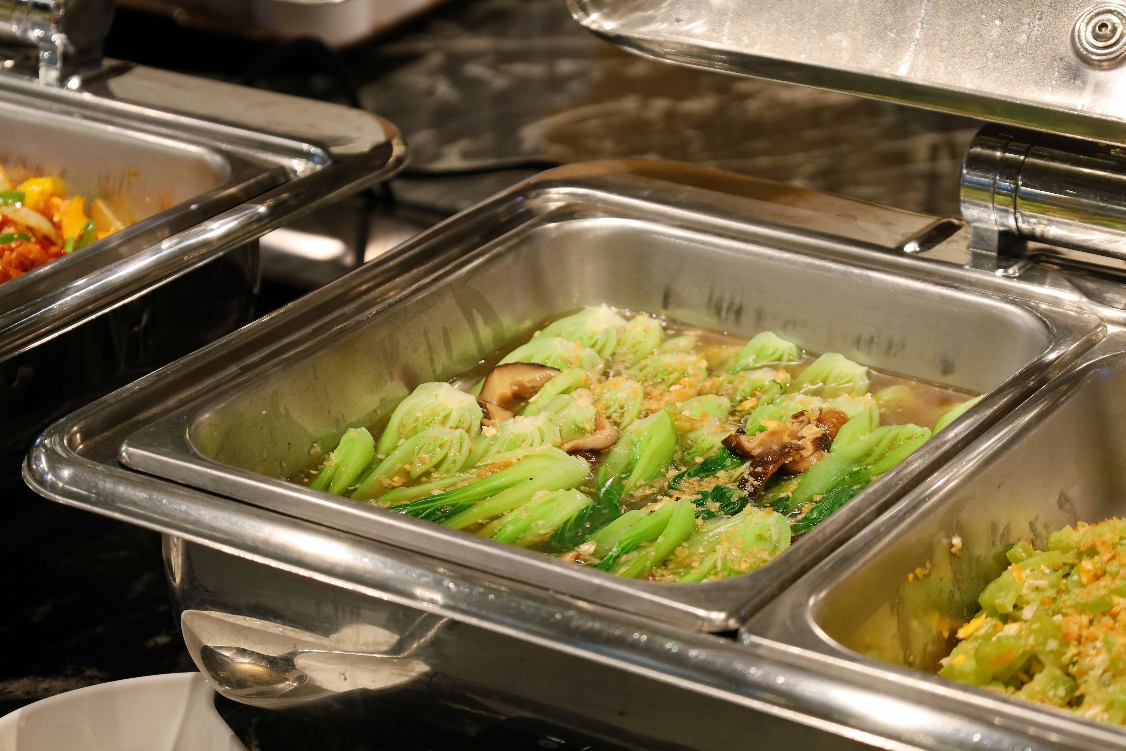 A buffet with various dishes, including a section with green vegetables and mushrooms.