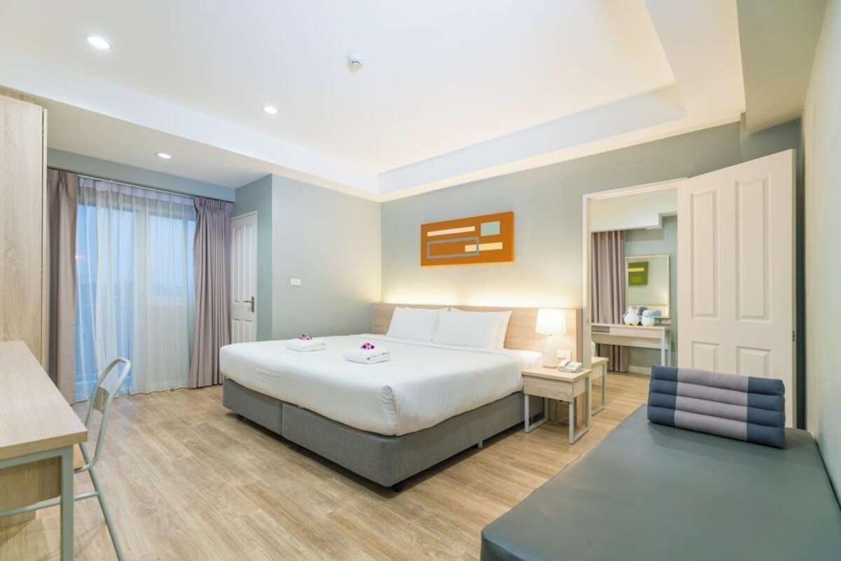 Een moderne hotelkamer met een groot bed, nachtkastje en een klein zithoekje.