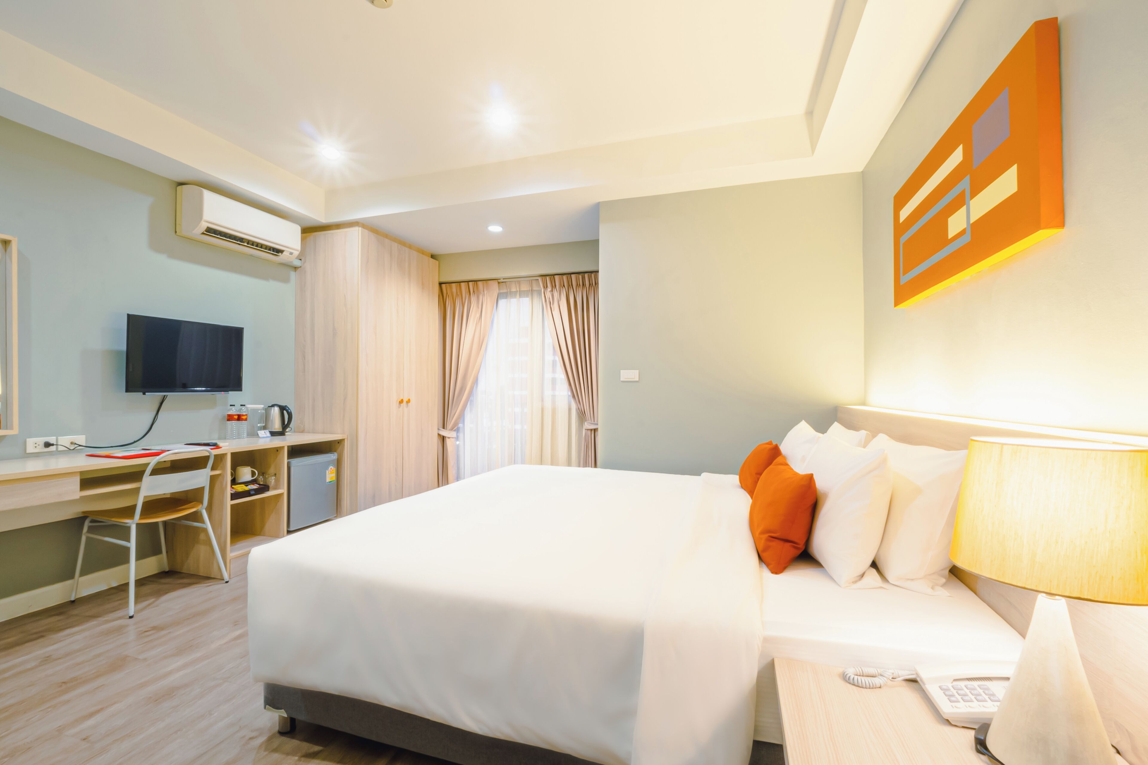 Een hotelkamer met een bed, bureau, stoel, televisie en een raam met gordijnen.