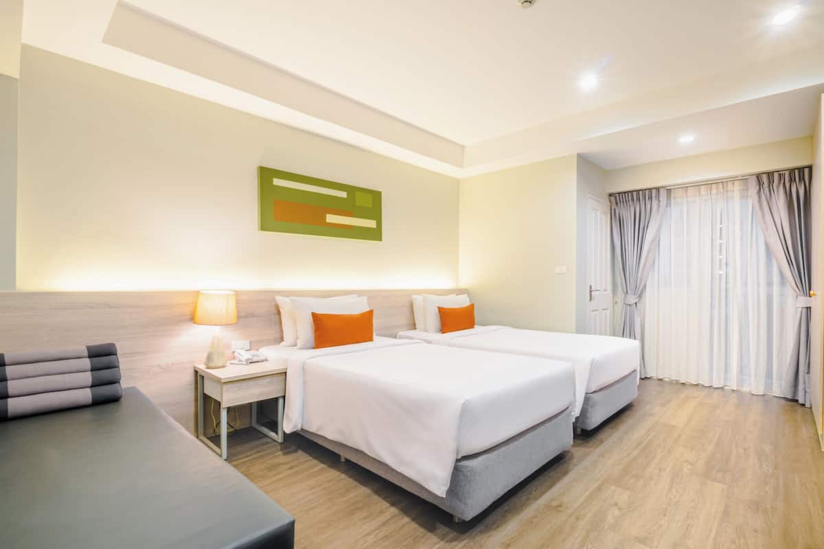 Une chambre d’hôtel avec deux lits, un bureau, une lampe et une fenêtre avec des rideaux.