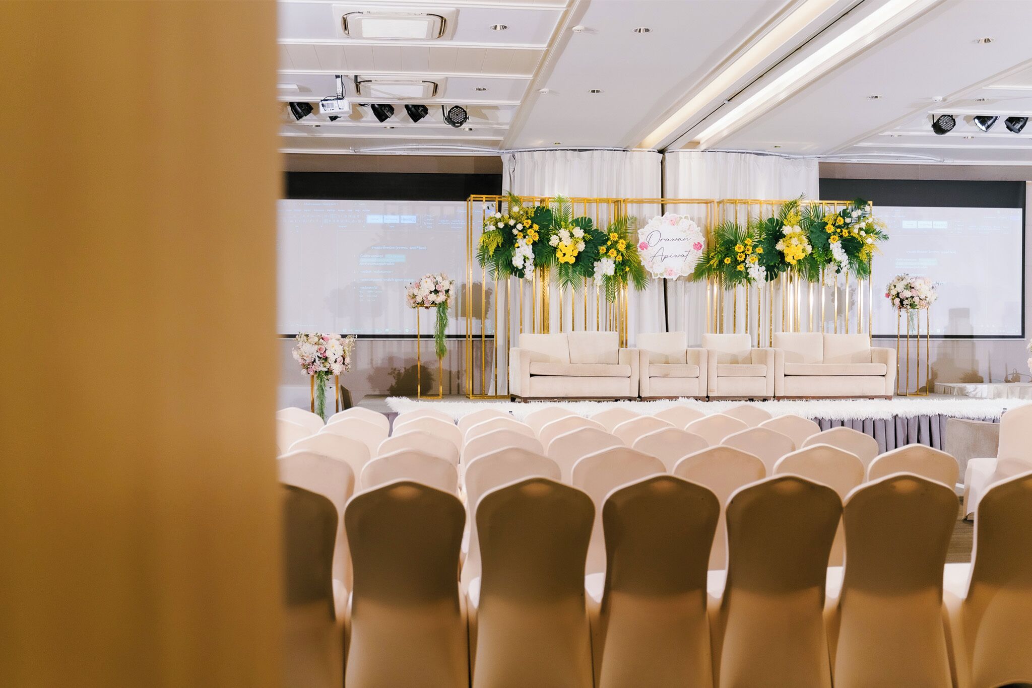 A conference room with rows of chairs, a stage with floral decorations, and a projector screen.