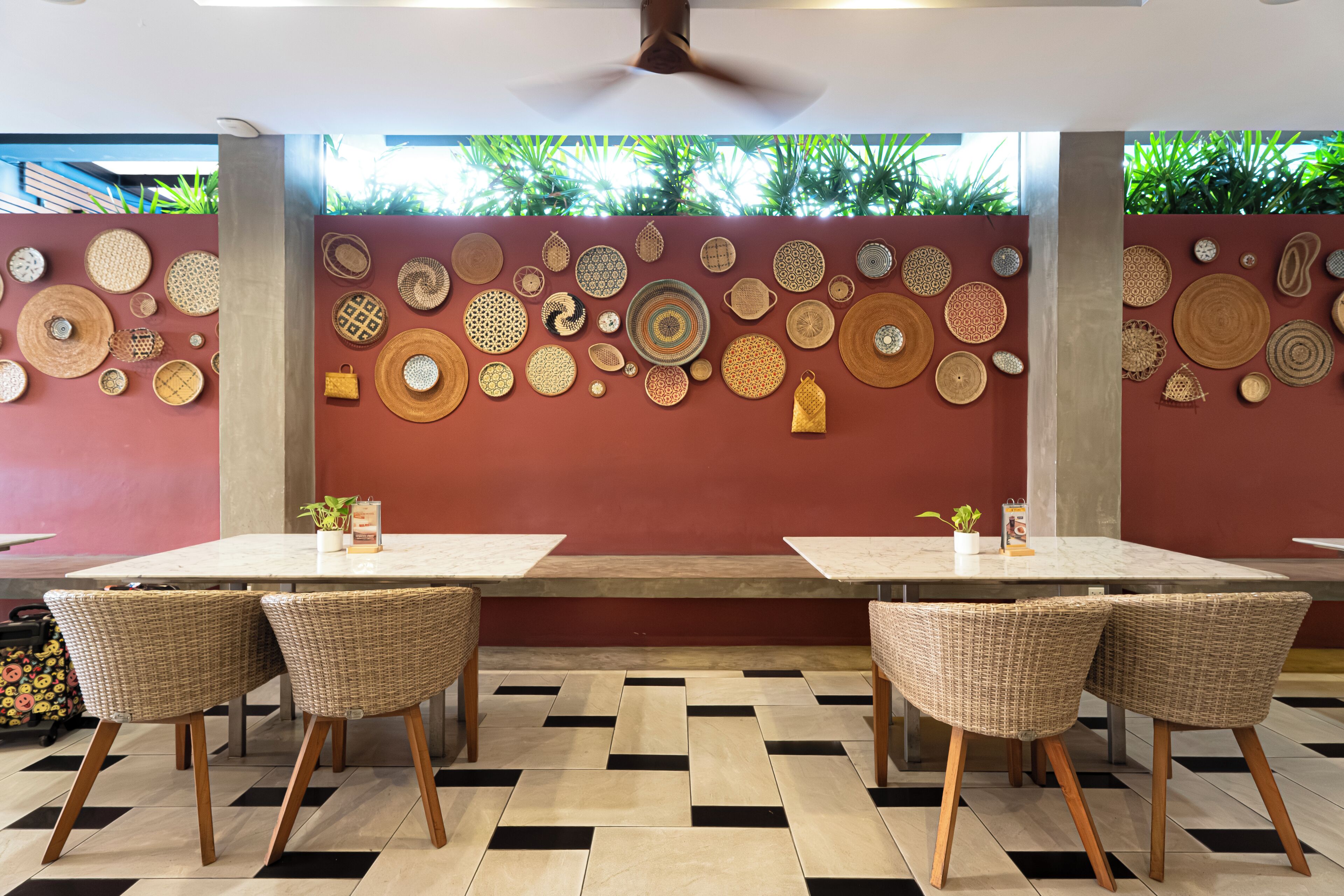 A restaurant with a checkered floor, wicker chairs, and a wall decorated with various woven items.