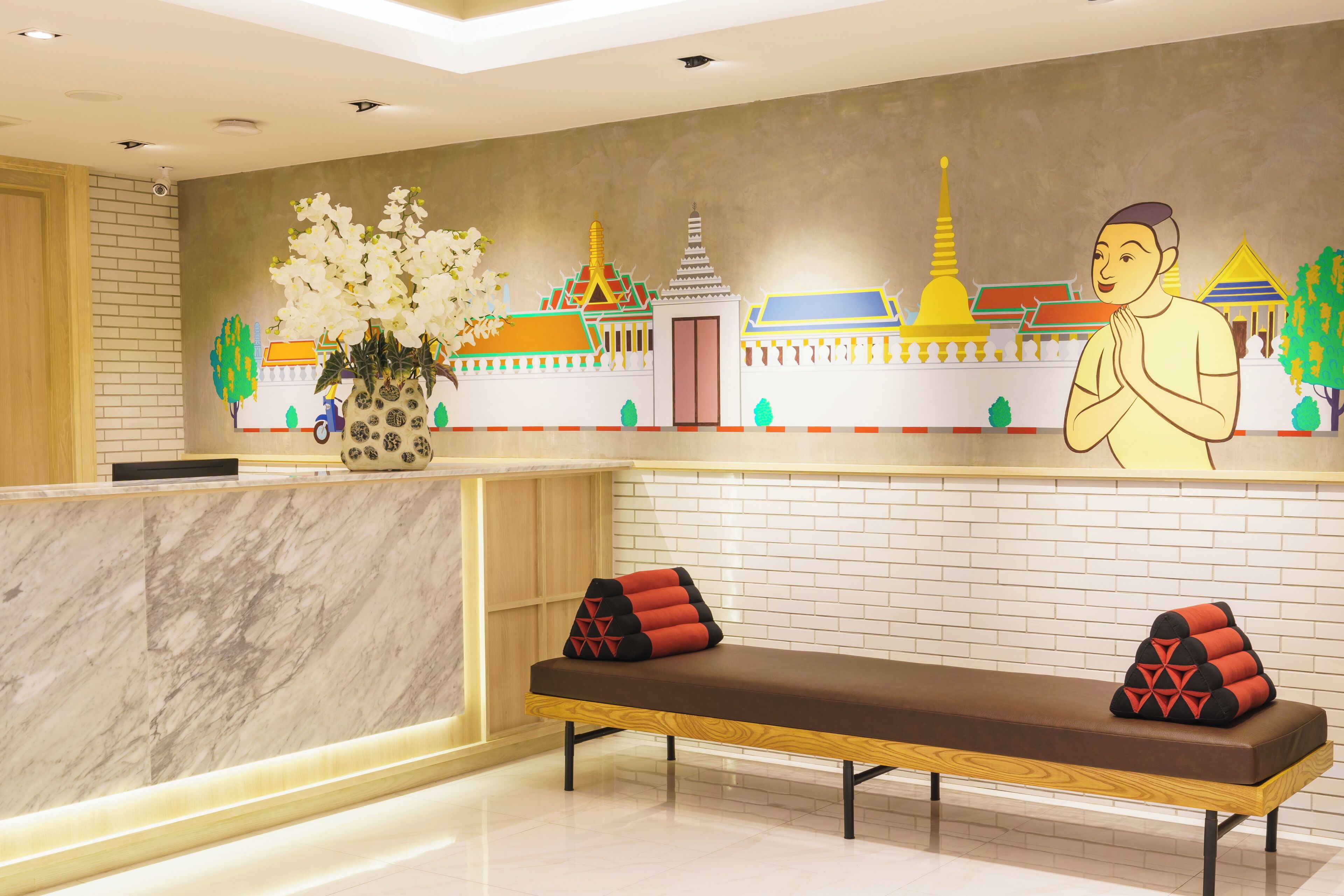 A reception area with a marble counter, a bench with red and black cushions, and a mural of a temple and a person in traditional attire.