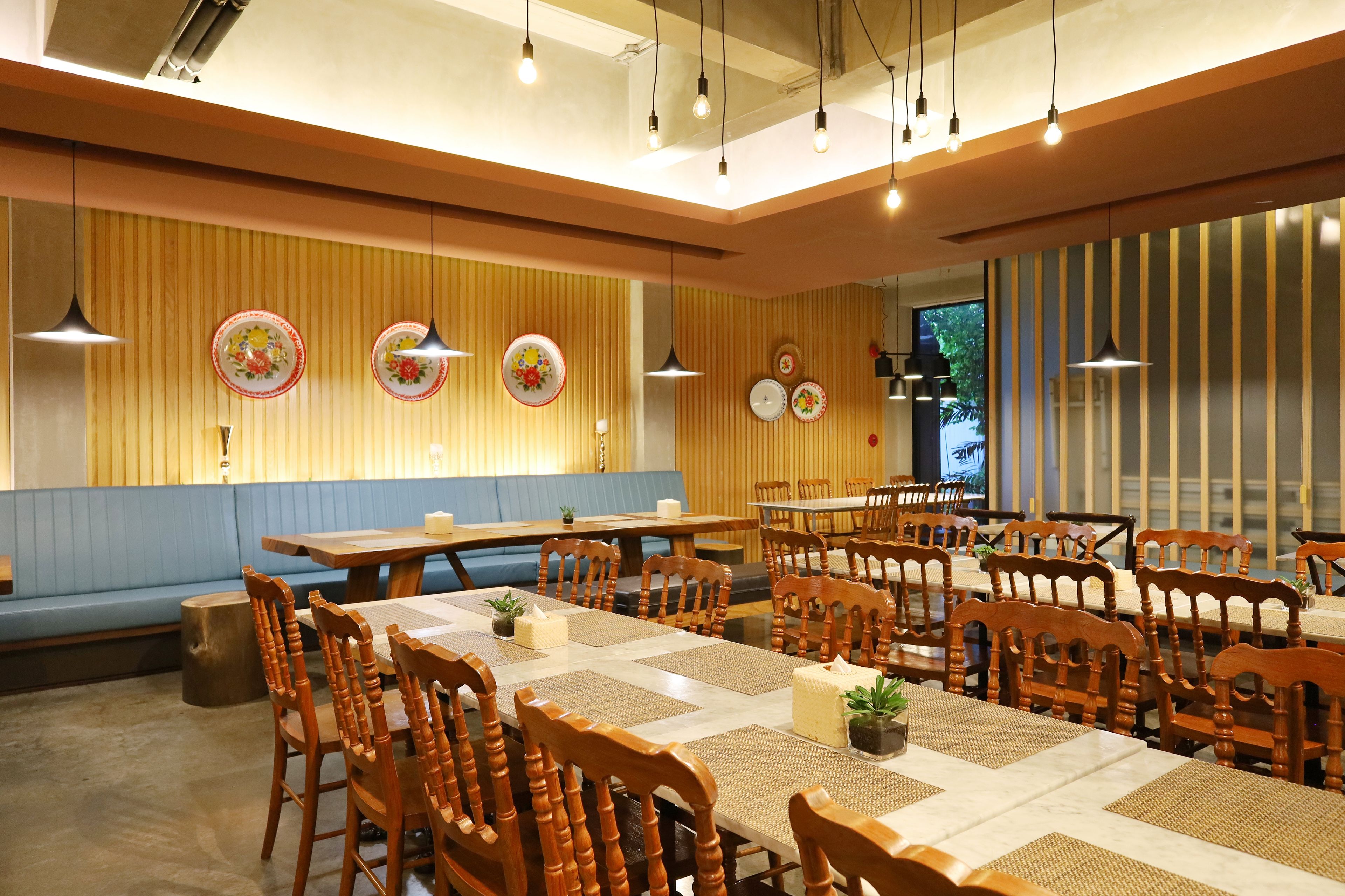Un restaurante con mesas y sillas de madera, un banco tapizado de azul y platos decorativos en la pared.