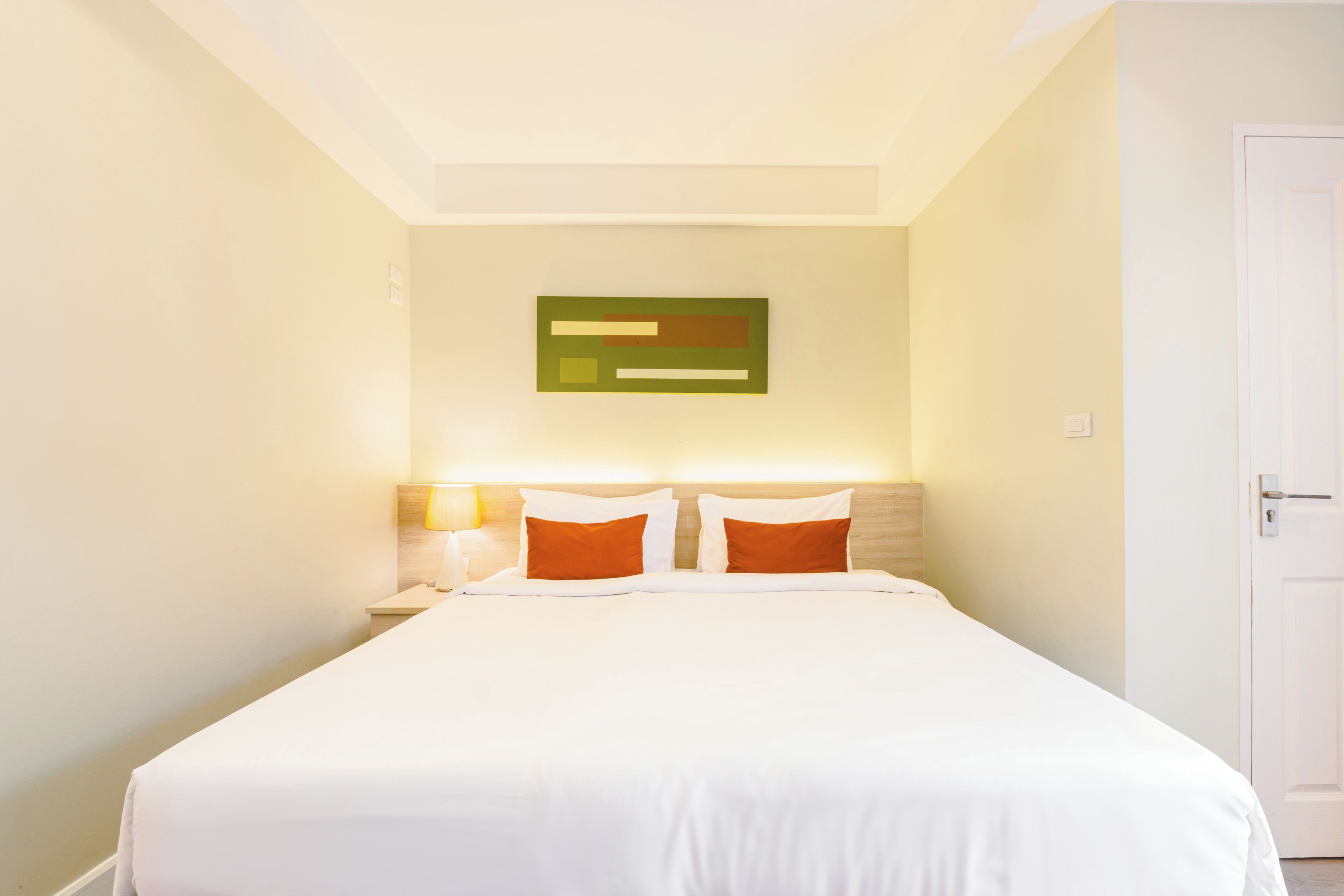 A hotel room with a bed, a nightstand, a wall-mounted light, and a door.