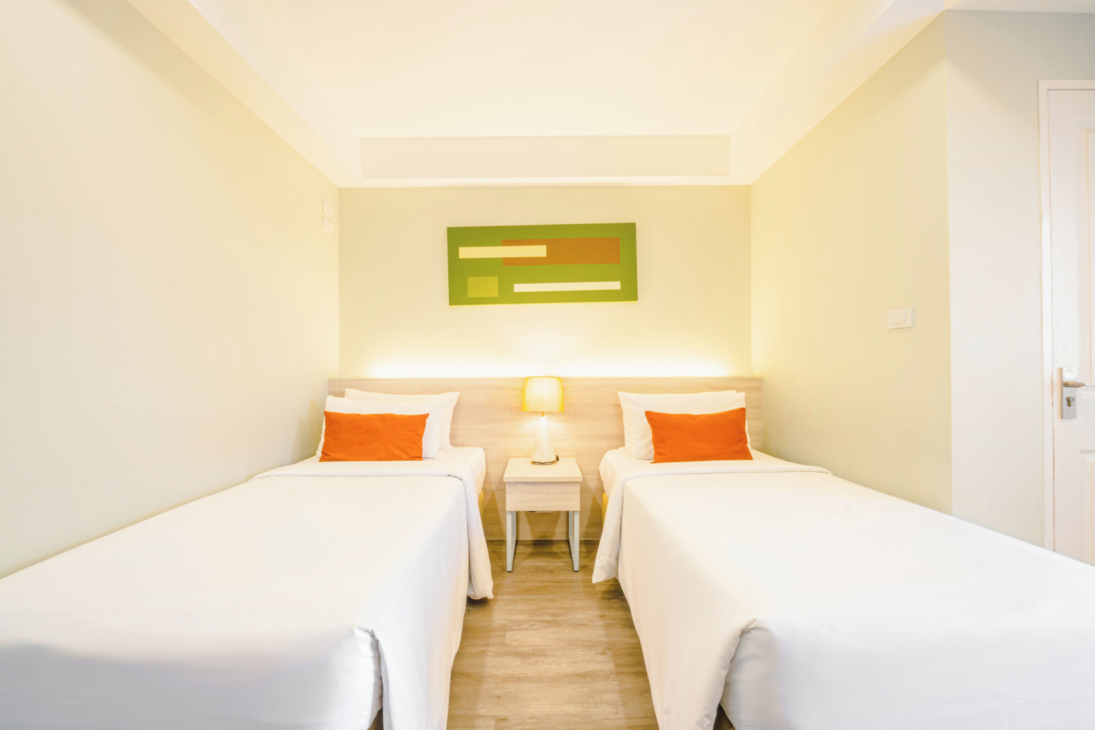 Habitación de hotel con dos camas individuales, una mesita de noche con lámpara y una obra de arte colgada en la pared.