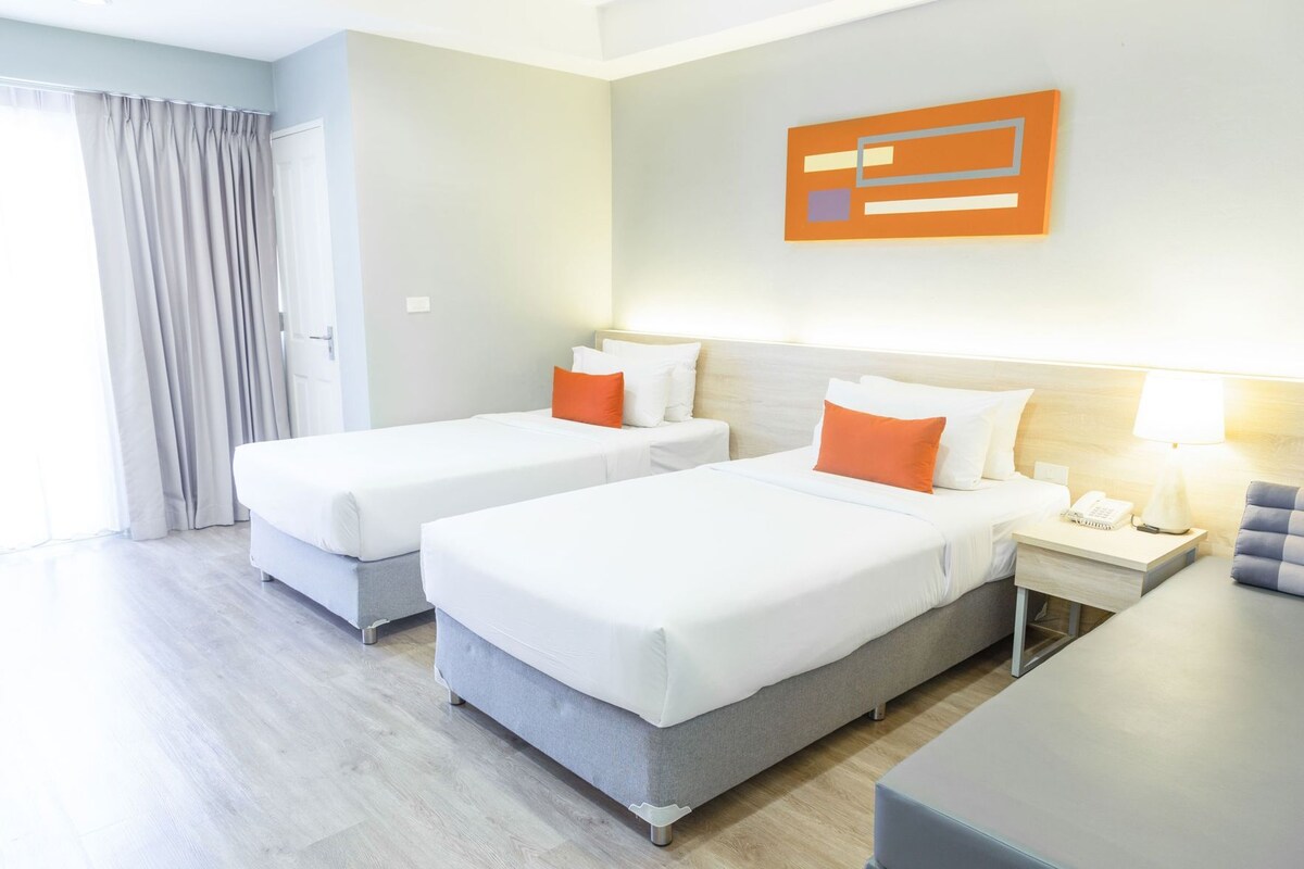 Una habitación de hotel con dos camas, un escritorio, una silla, una lámpara y un cuadro en la pared.