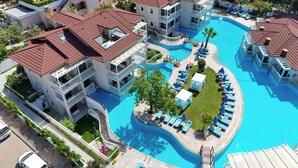 Ett hotellkomplex med flera byggnader, en central pool och utomhusområden med sittplatser.
