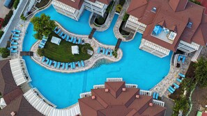 An aerial view of a resort with a large central swimming pool, multiple guest rooms, and a well-maintained lawn area.