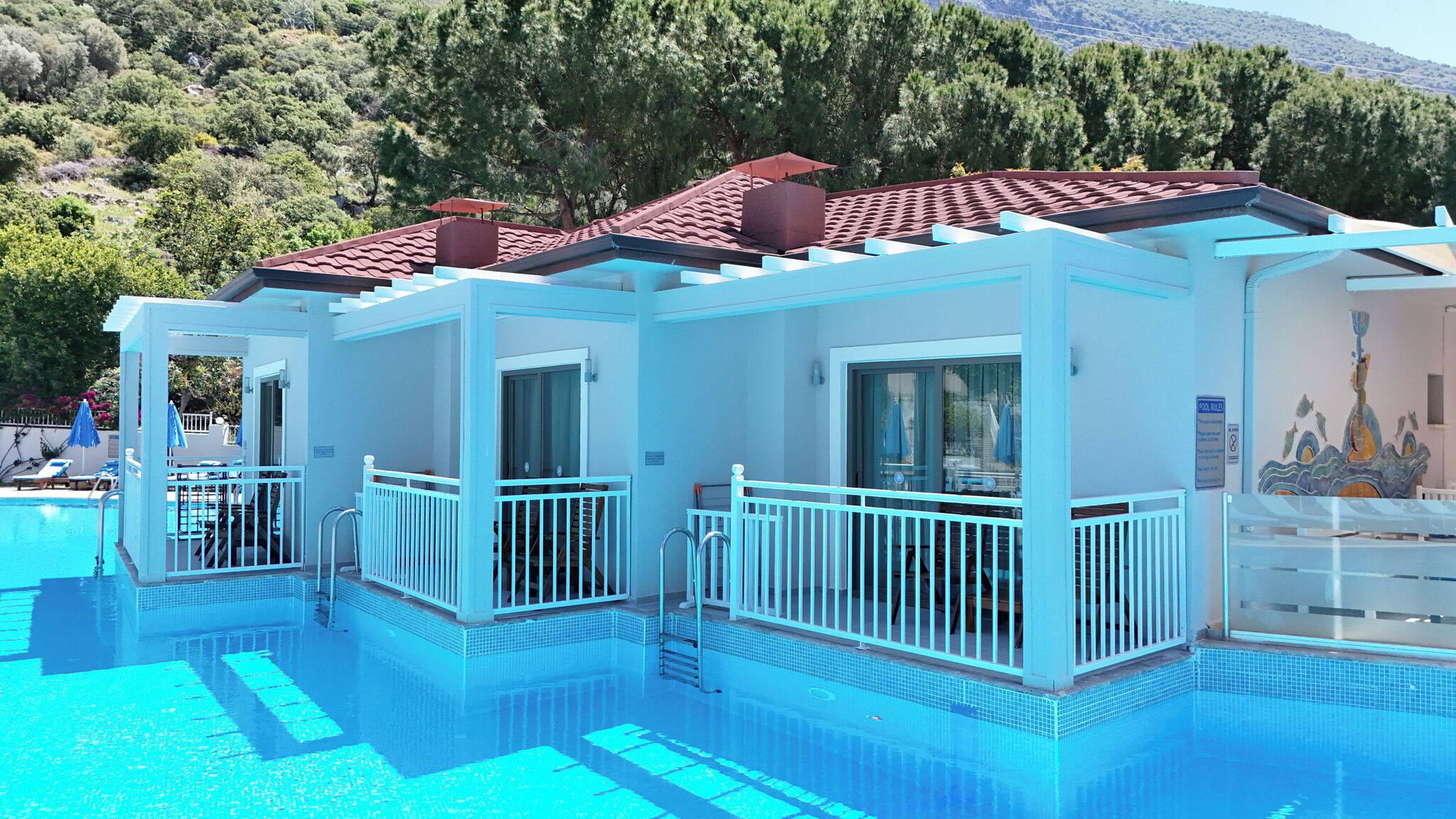 A poolside building with a red-tiled roof, glass doors, and a pool with clear blue water.