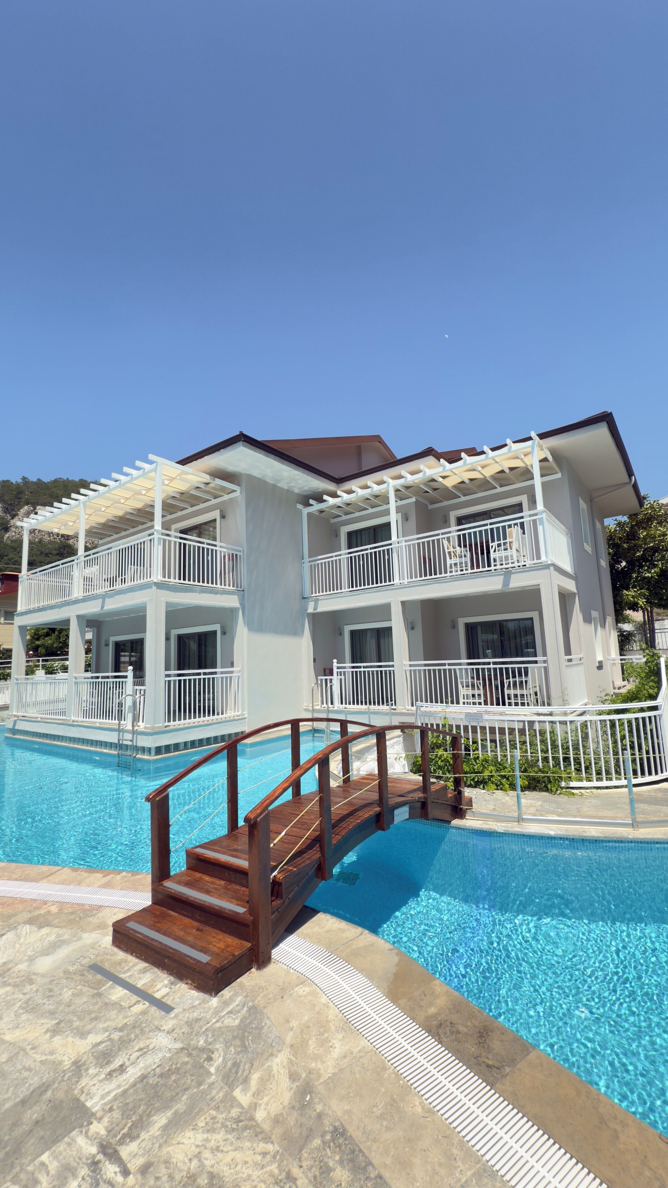Un edificio de dos pisos con balcones, piscina y un puente de madera.