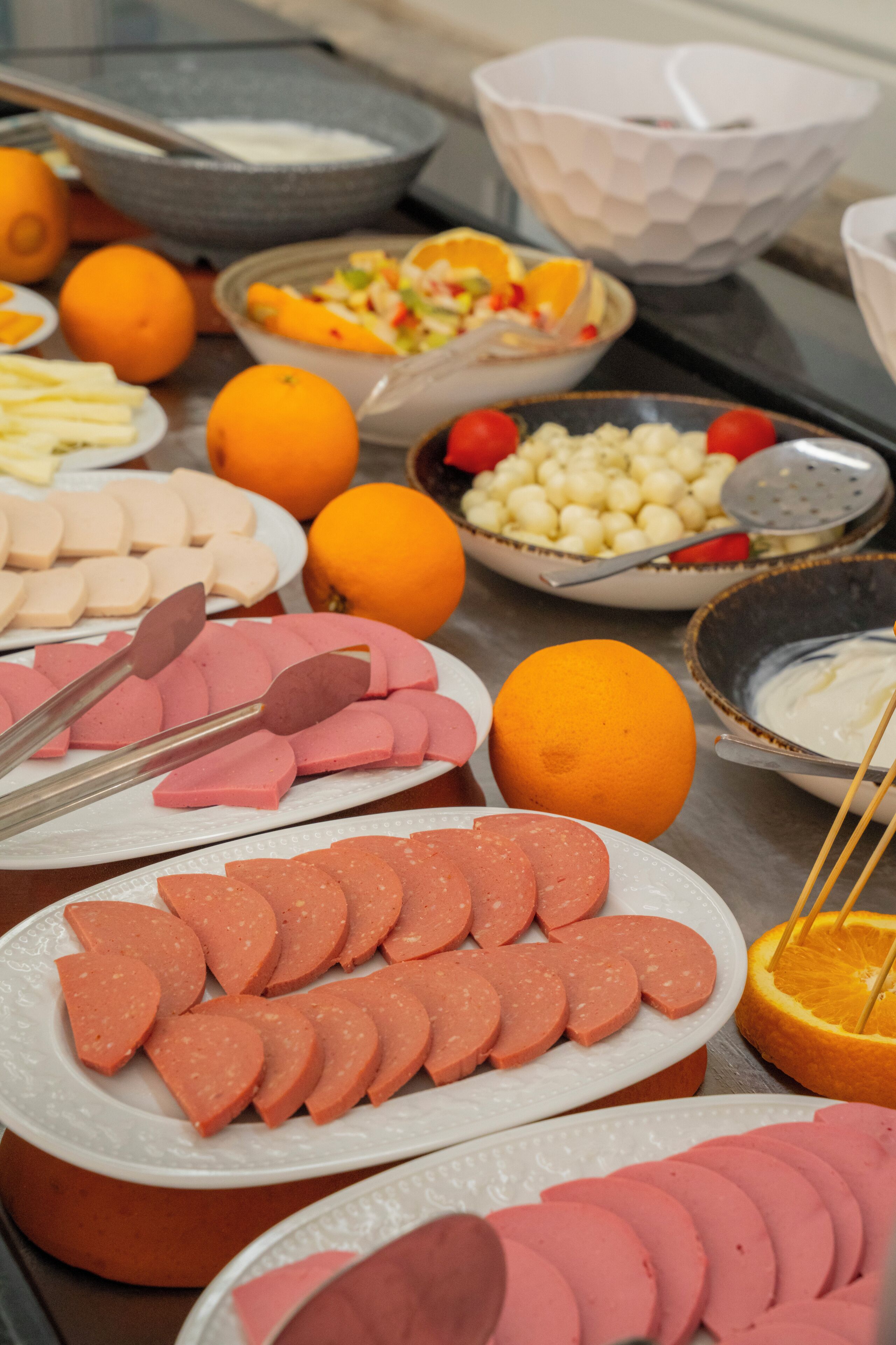 Una mesa de buffet con diversos alimentos, entre ellos, carnes cortadas, frutas y verduras.