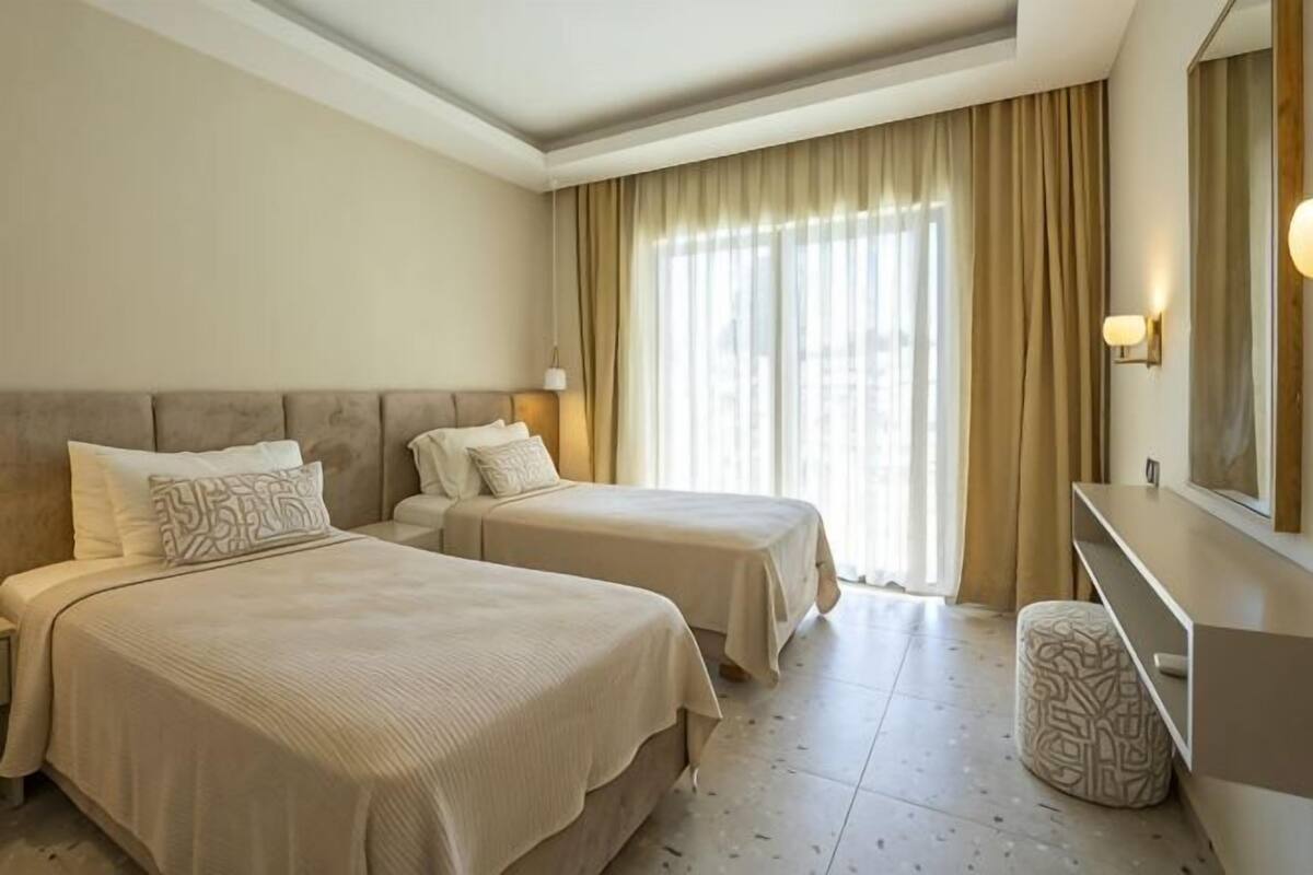 Een hotelkamer met twee bedden, een kaptafel met spiegel en een groot raam met gordijnen.