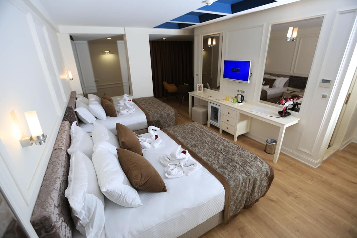A hotel room with two beds, a desk, a mirror, and a television.