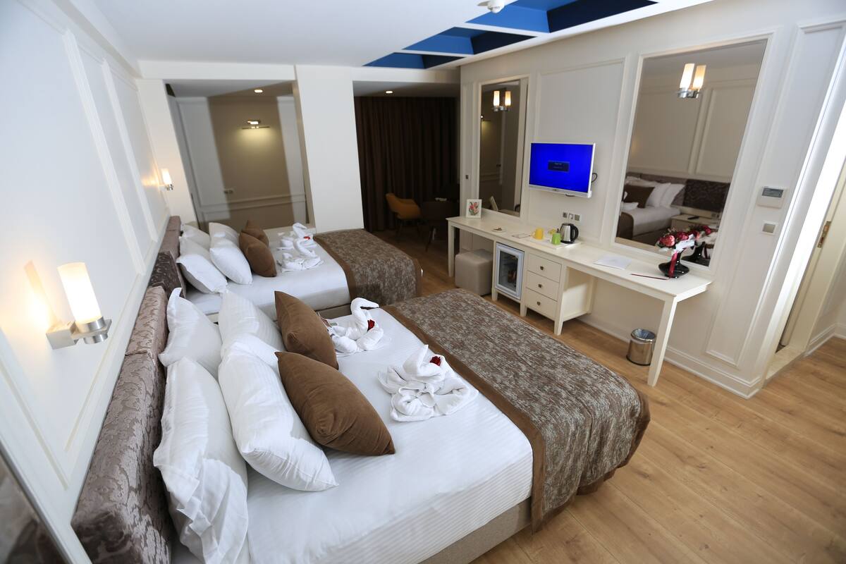 A hotel room with two beds, a desk, a mirror, and a television.