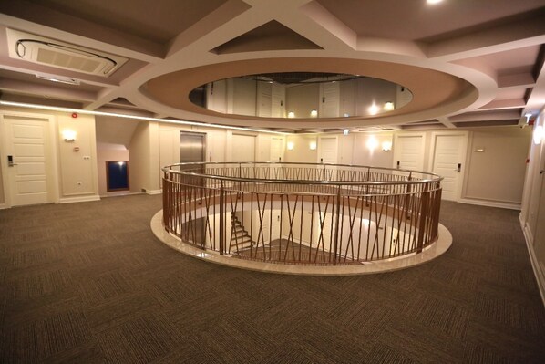 A spacious, circular atrium with a central staircase, multiple doors, and a modern ceiling design.