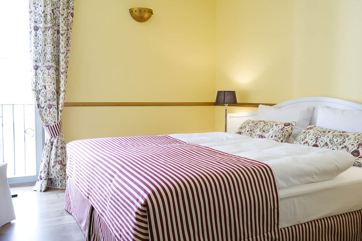 A neatly made bed with striped bedding, a bedside lamp, and a floral-patterned pillow.