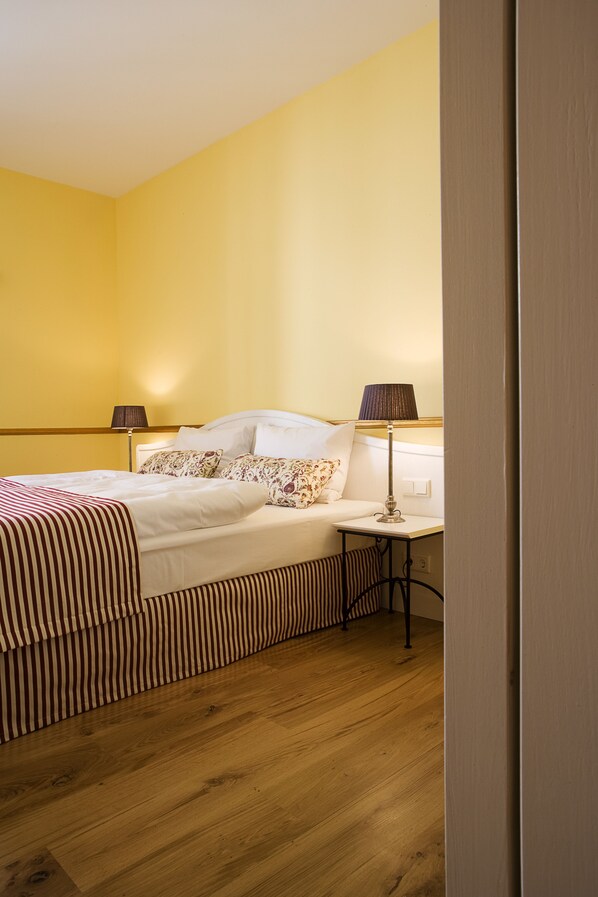 Una camera d'albergo con un letto, abat-jour e pavimento in legno.