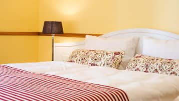 A hotel room with a bed, floral-patterned pillows, a lamp, and a striped blanket.