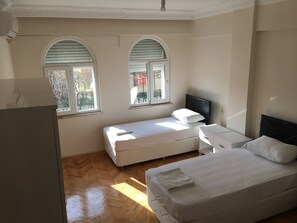 Un dormitorio con dos camas, un aparador blanco y dos ventanas con contraventanas.