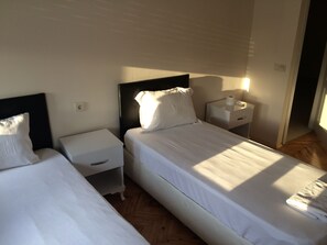 Una habitación de hotel con dos camas, una mesita de noche con lámpara y suelo de madera.