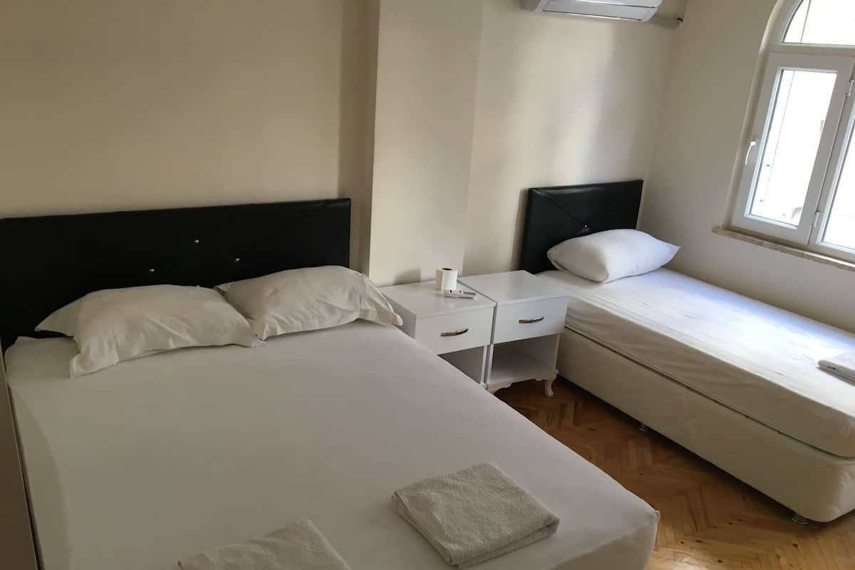Une chambre avec un grand lit, un plus petit lit, une table de chevet et une fenêtre.