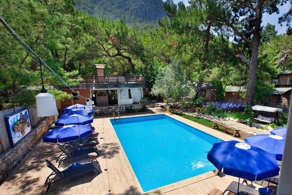 Una piscina con sombrillas azules, sillas de descanso y una cubierta de madera.