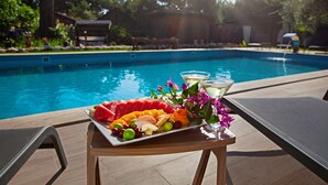 Una mesa junto a la piscina con una bandeja de frutas, una copa de martini y un arreglo floral.