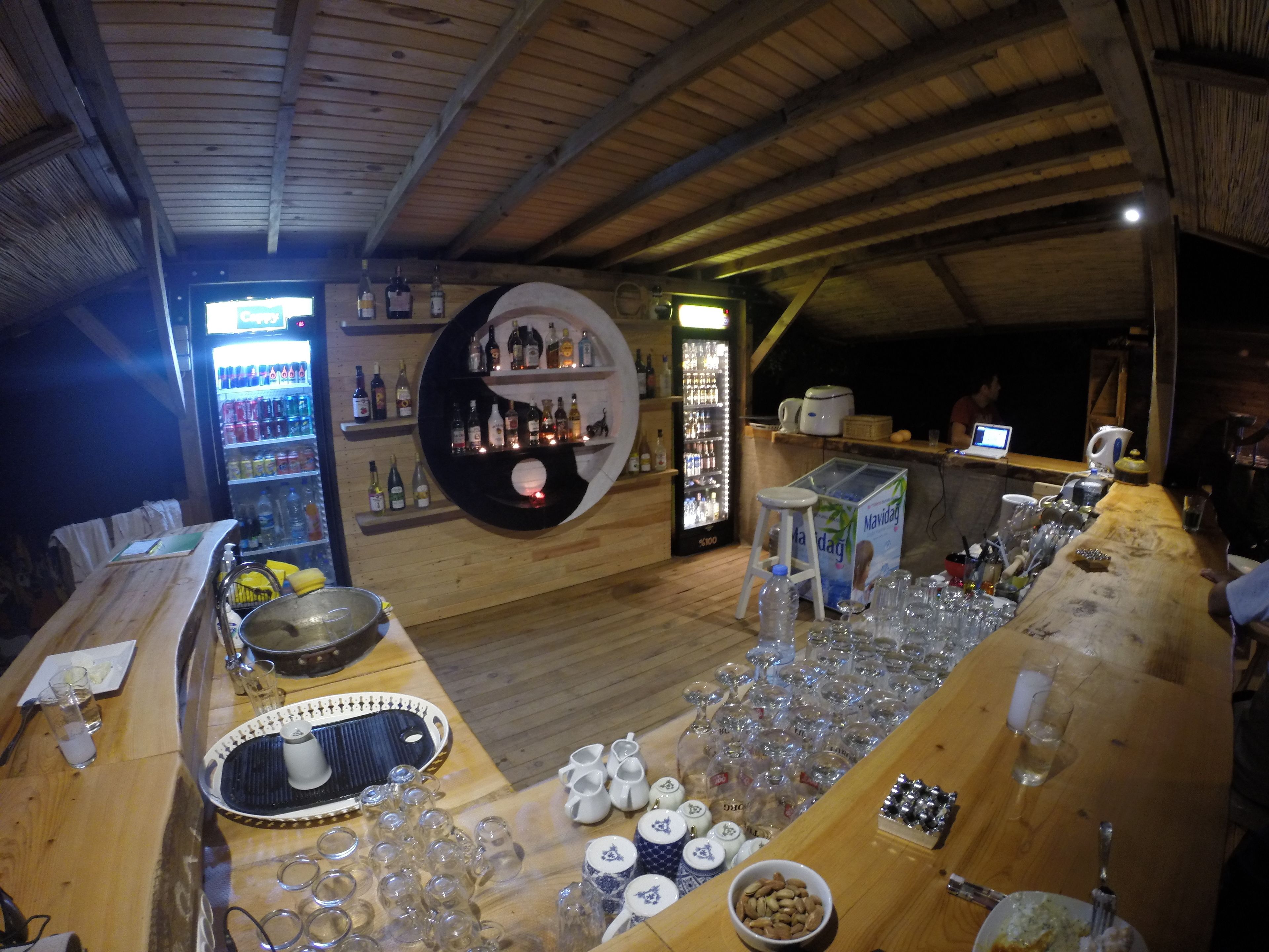 A bar area with wooden furniture, a refrigerator stocked with beverages, and a variety of glassware and bottles.