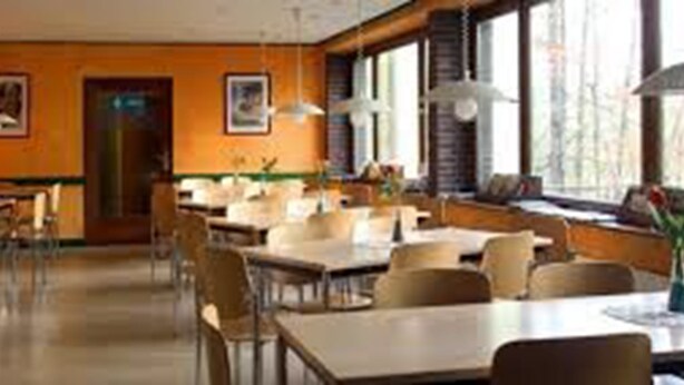 Un comedor espacioso con varias mesas y sillas, ventanas amplias y lámparas colgantes.