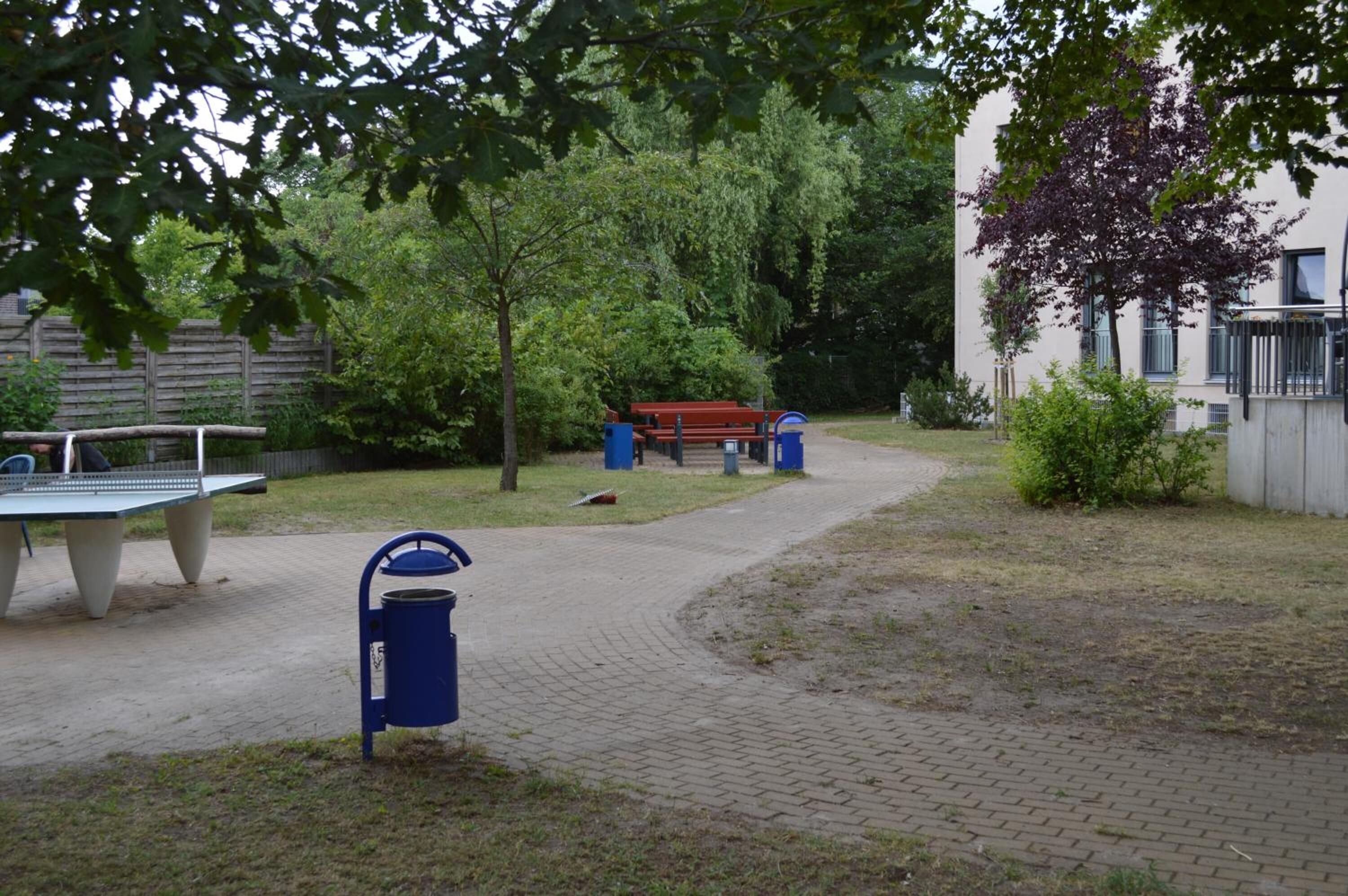 A park area with a ping pong table, benches, and trash bins.