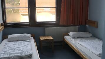 A dormitory room with two single beds, a wooden table, and a chair.