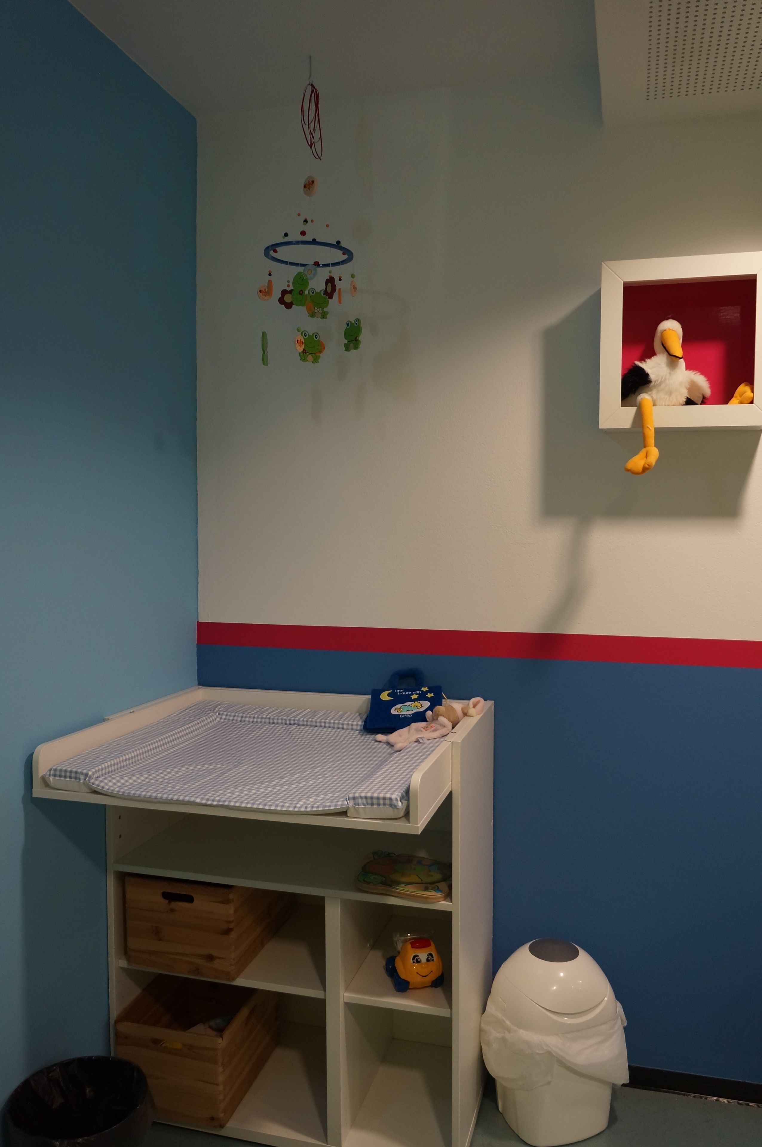 Ein Kinderzimmer mit einem Etagenbett, einem kleinen Regal voll Spielzeug, einer hängenden Dekoration und einem Mülleimer.