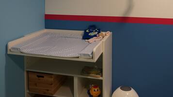 Ein Kinderzimmer mit einem Etagenbett, einem kleinen Regal voll Spielzeug, einer hängenden Dekoration und einem Mülleimer.