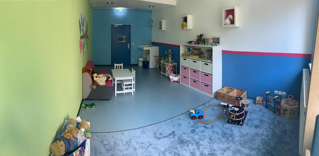Un cuarto de juegos infantil con una pared azul, una mesa blanca y un mueble de almacenamiento rosa.