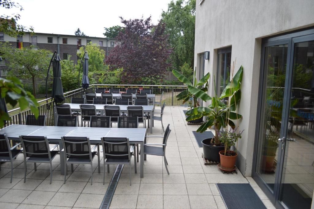 Un patio al aire libre con mesas y sillas, plantas en macetas y un edificio con ventanas amplias.