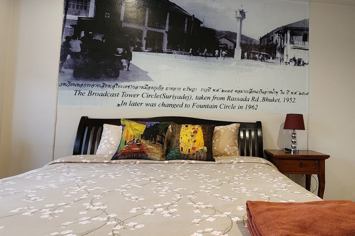 Ein Schlafzimmer mit einem Bett, einem Nachttisch, einer Lampe und einer Wand mit einem historischen Foto und Text.