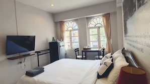 A hotel room with a bed, a TV, a desk, and two windows with curtains. - Machima House (Phuket)