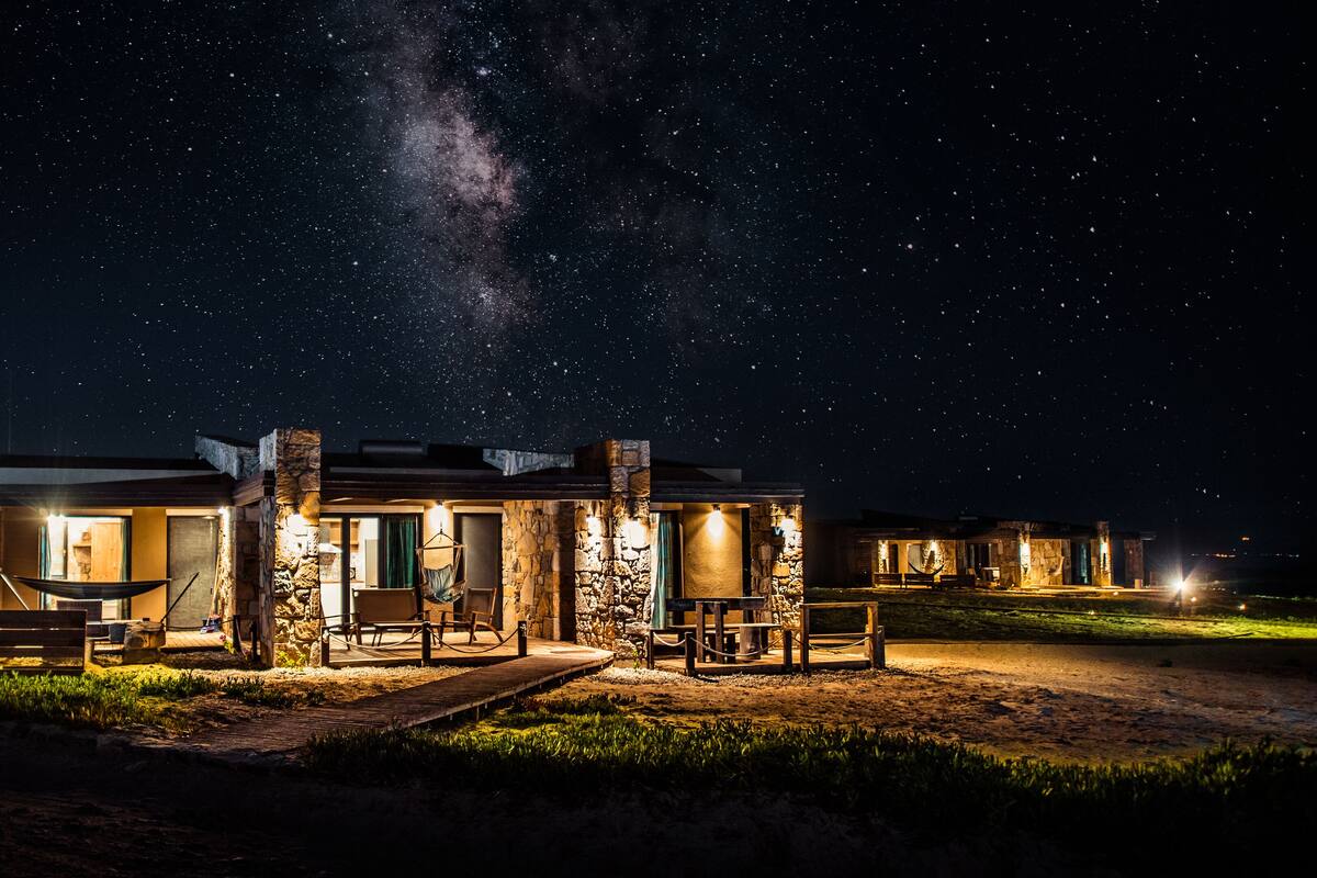 A two-story lodge with stone walls and a wooden deck, under a starry night sky.